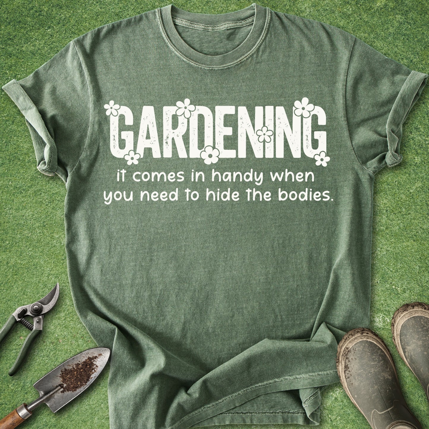 Green t-shirt with humorous gardening text on a green background with gardening tools and boots.