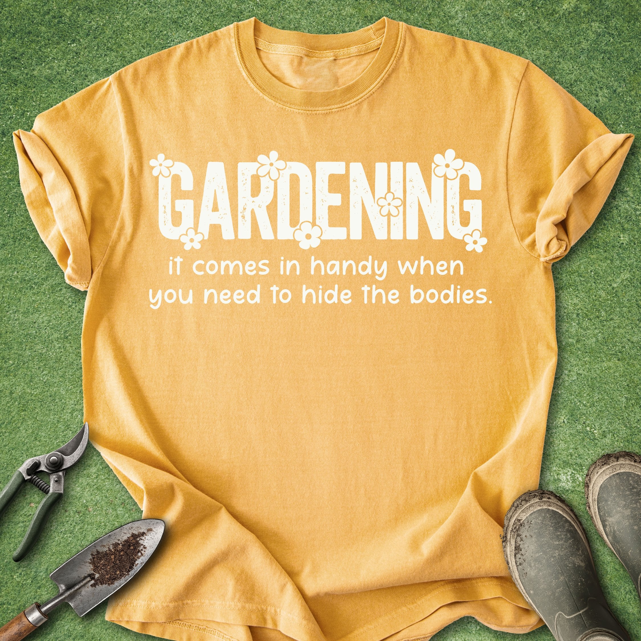 Yellow t-shirt with humorous gardening text on a green background with gardening tools and boots.