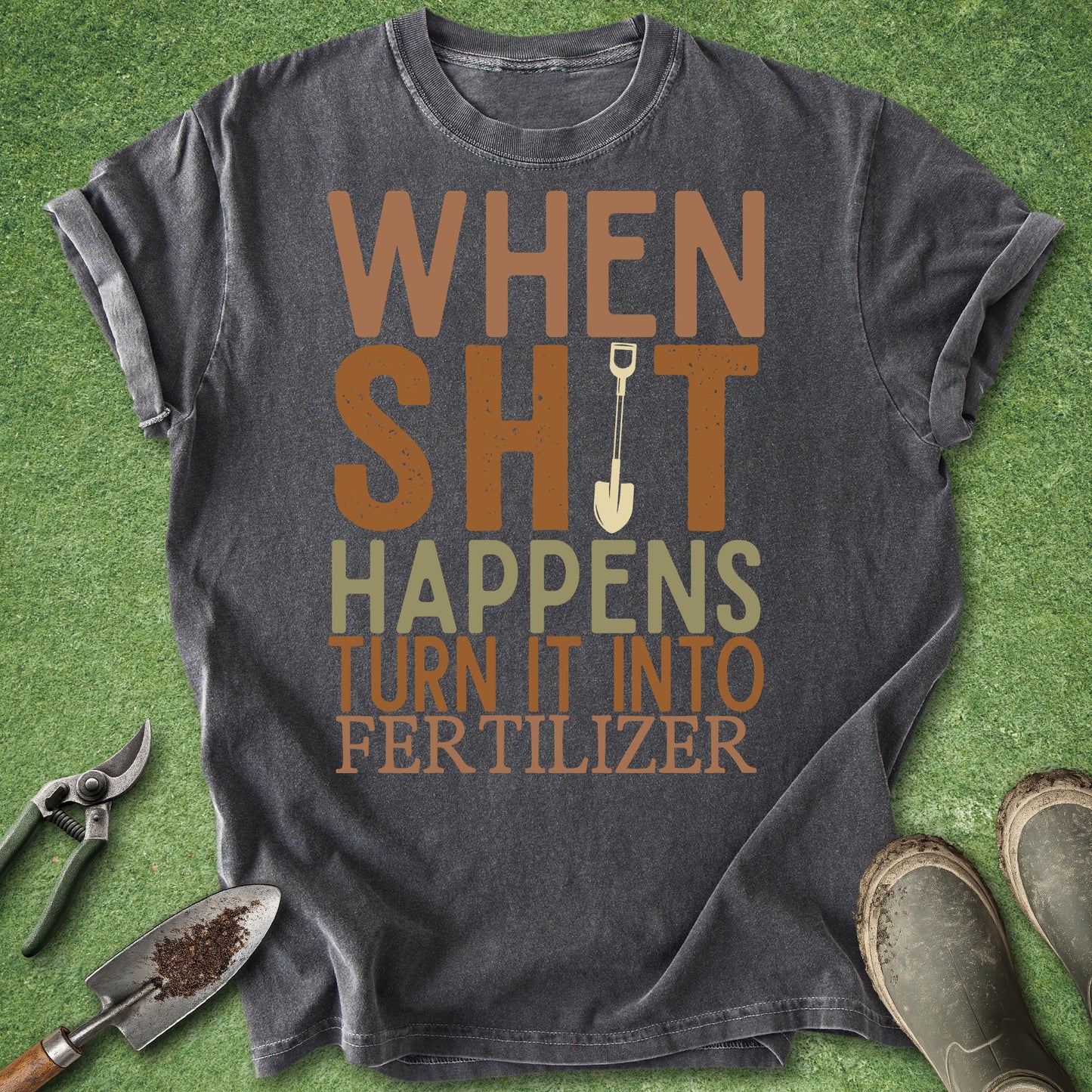 Gray t-shirt with humorous text on a green grass background with gardening tools.