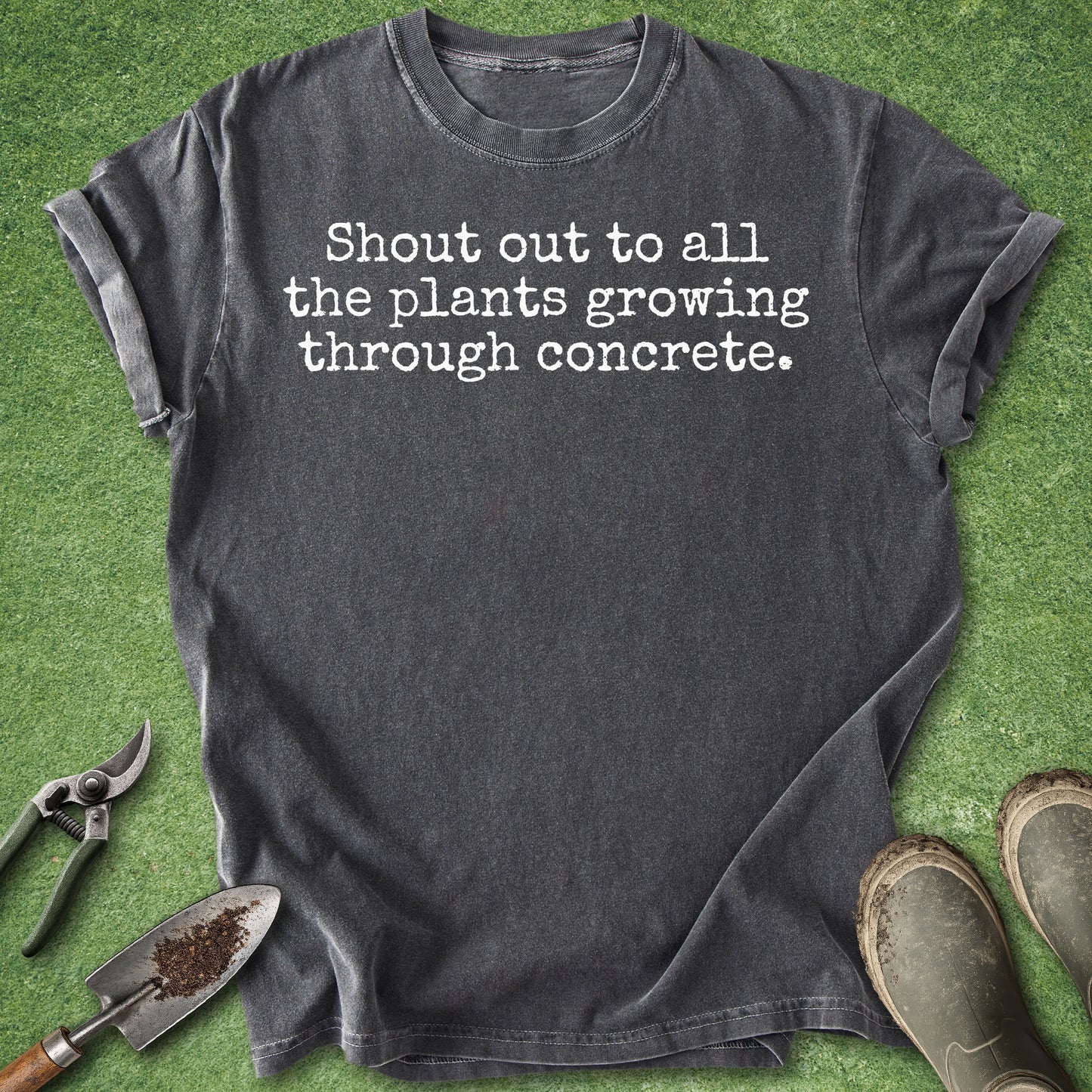 Comfort Colors pepper t-shirt featuring the phrase "Shout out to all the plants growing through concrete." in a minimalist white typewriter-style font.