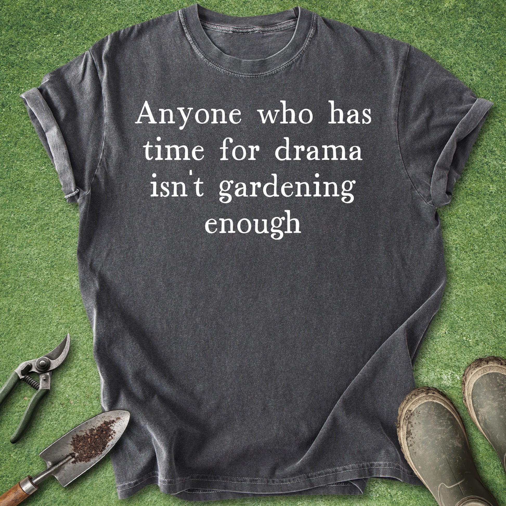 Gray t-shirt with humorous text on a green grass background with gardening tools.