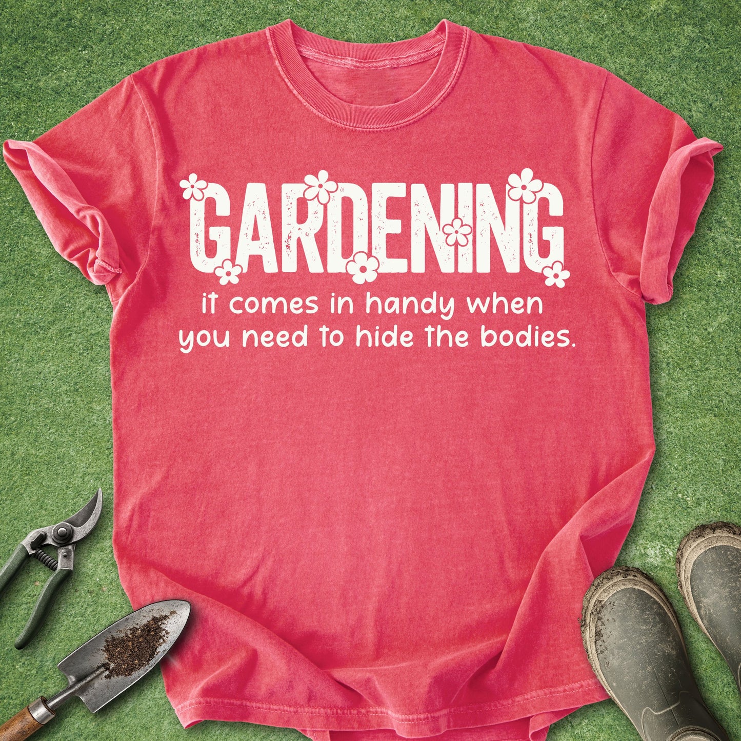 Red t-shirt with humorous gardening text on a grass background with gardening tools and boots.