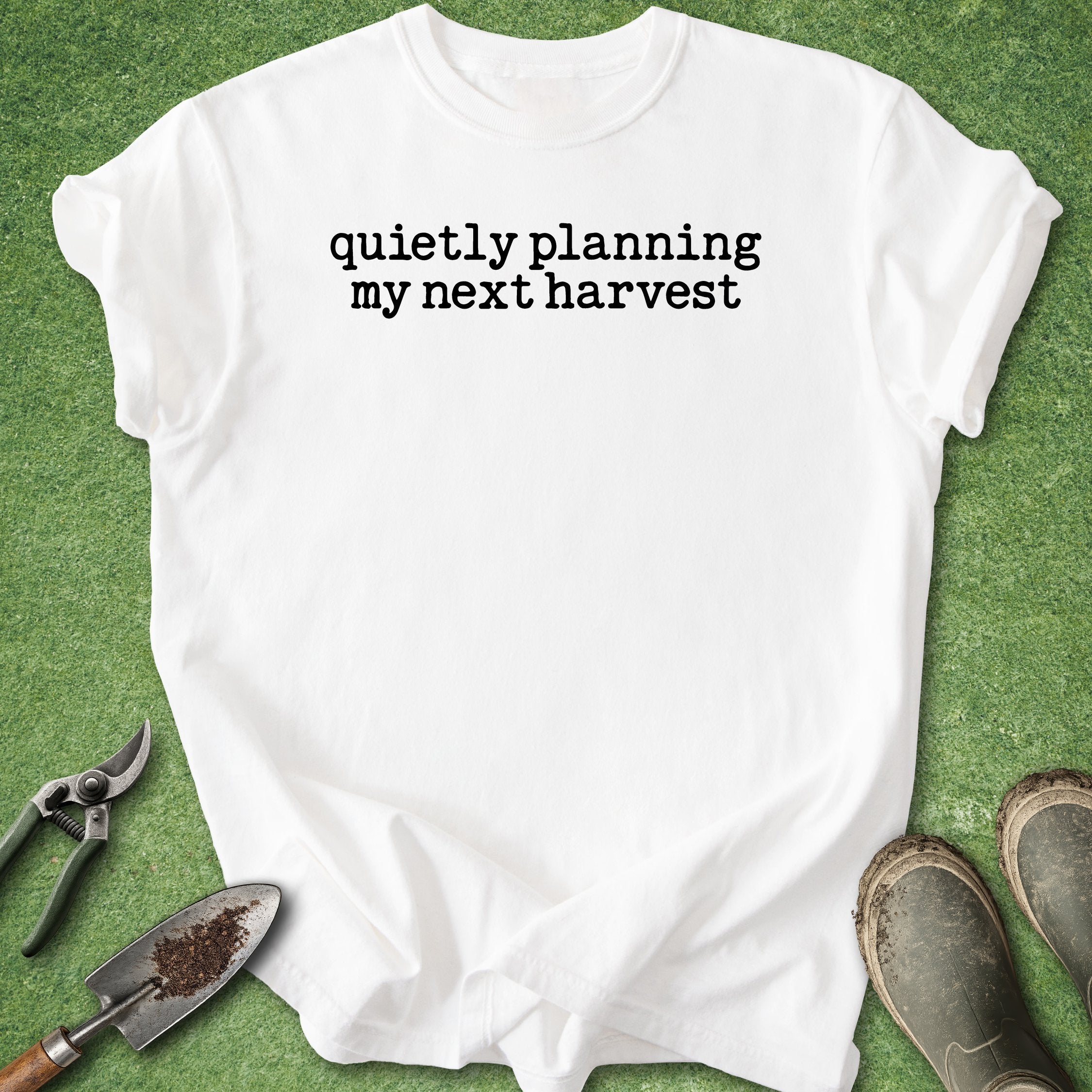 White t-shirt with 'quietly planning my next harvest' text on a green background with gardening tools.