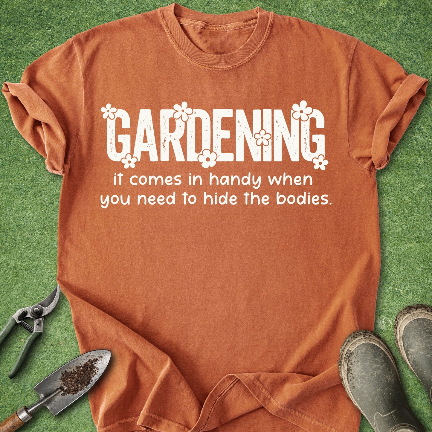Orange t-shirt with humorous gardening text on a grass background with gardening tools.