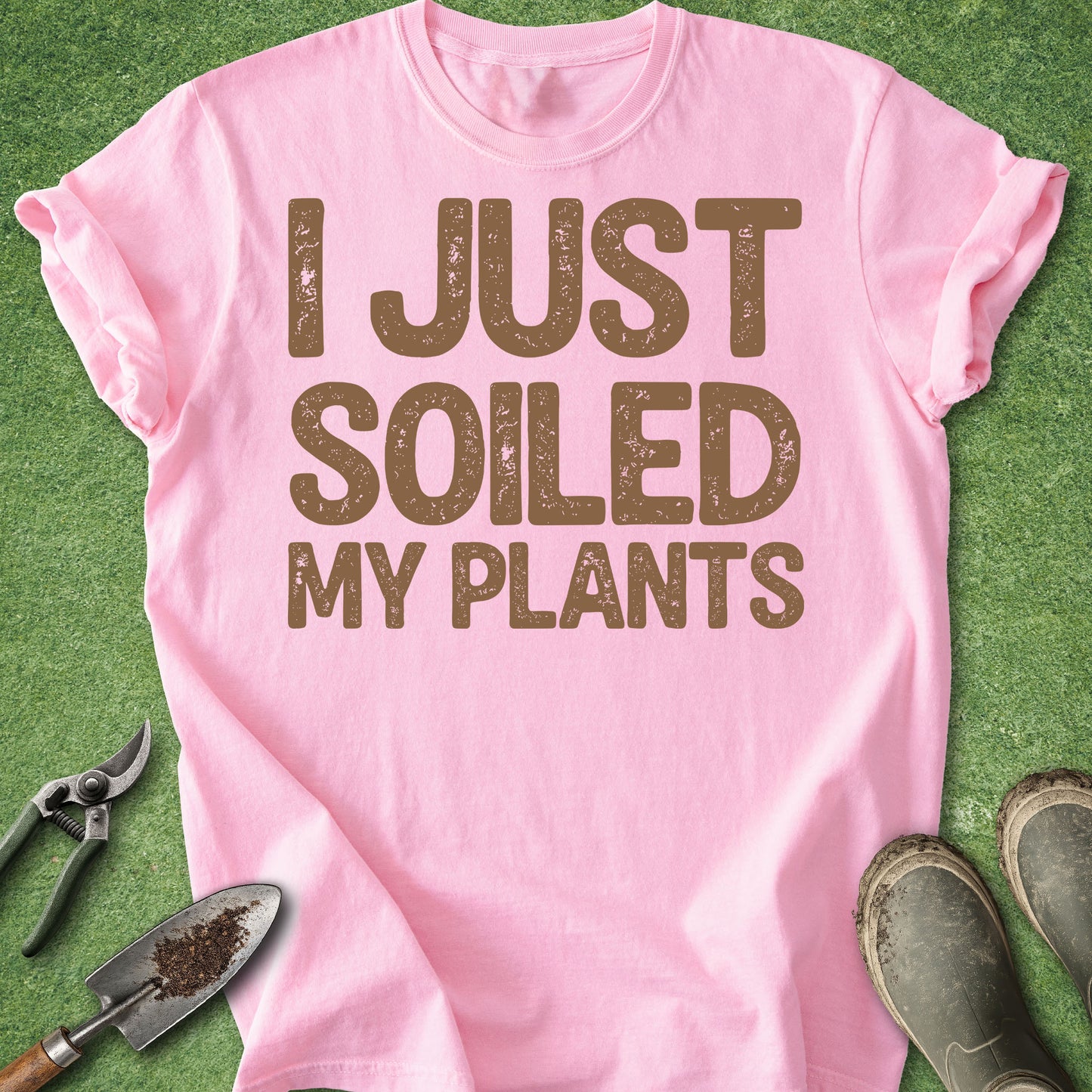 Pink t-shirt with 'I JUST SOILED MY PLANTS' text on a green background with gardening tools.