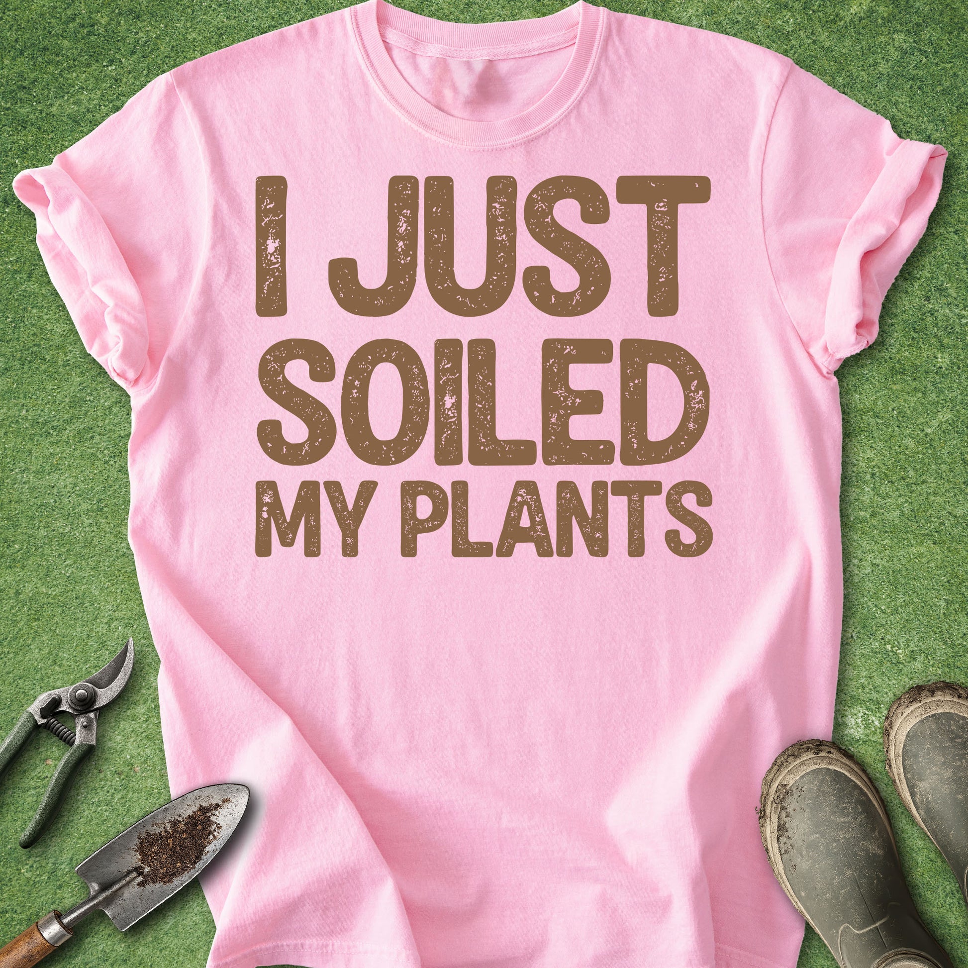 Pink t-shirt with 'I JUST SOILED MY PLANTS' text on a green background with gardening tools.