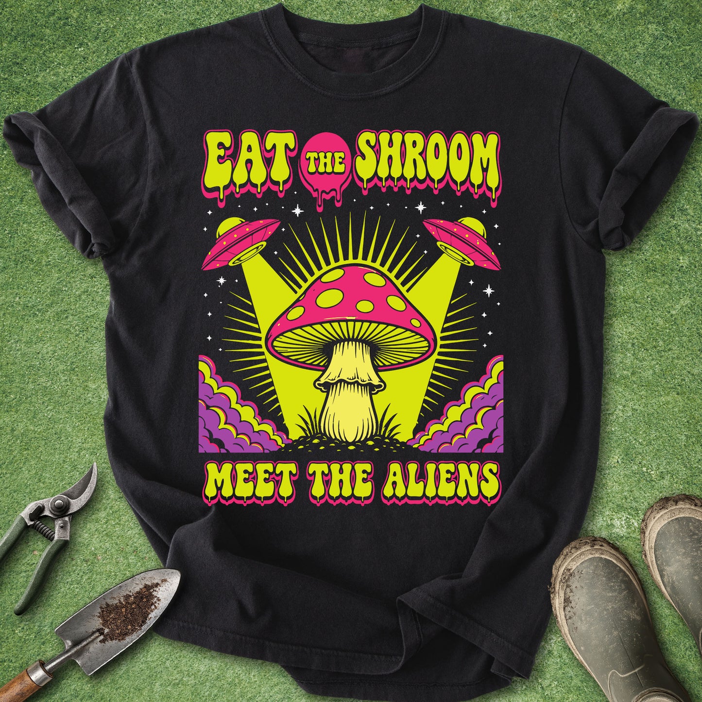 Comfort Colors black t-shirt featuring the phrase "Eat the Shroom Meet the Aliens" with a psychedelic mushroom, flying UFOs, neon colors, cosmic rays, and retro sci-fi artwork.
