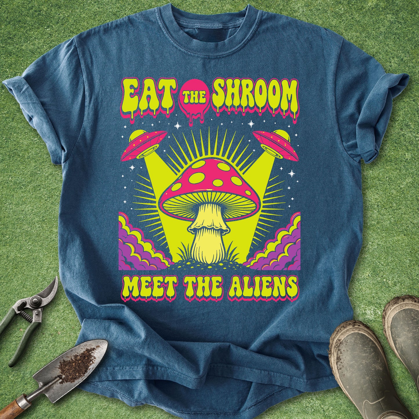 Comfort Colors midnight blue t-shirt featuring the phrase "Eat the Shroom Meet the Aliens" with a psychedelic mushroom, flying UFOs, neon colors, cosmic rays, and retro sci-fi artwork.