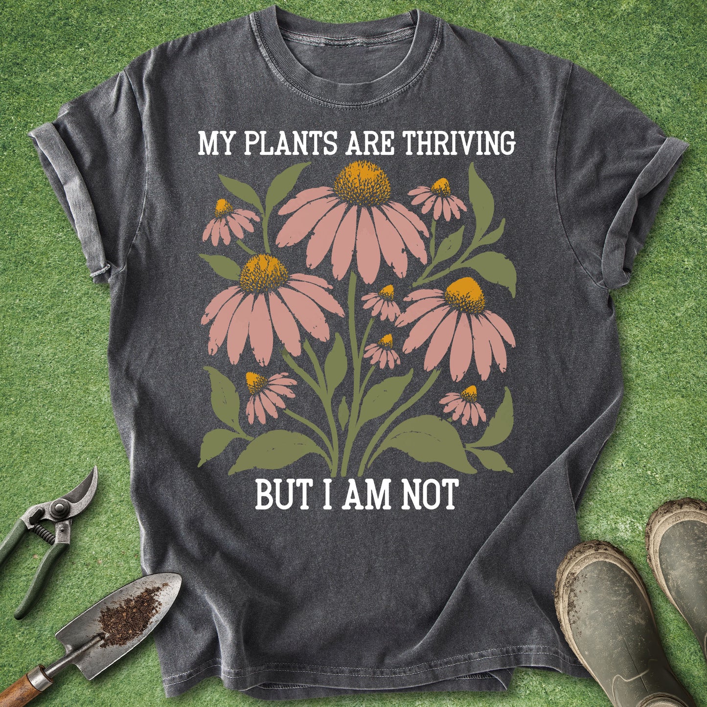 Pepper colored t-shirt featuring pink coneflowers with green leaves and the text “My Plants Are Thriving But I Am Not.”