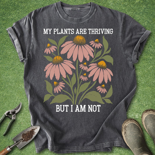 Pepper colored t-shirt featuring pink coneflowers with green leaves and the text “My Plants Are Thriving But I Am Not.”