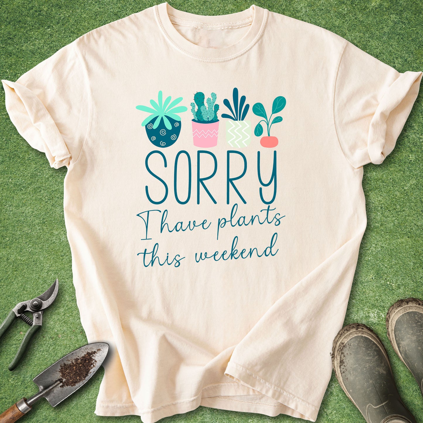 Beige t-shirt with plant-themed text on a green surface with gardening tools.