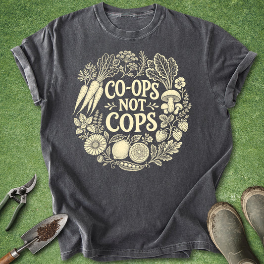 Vintage botanical gardening t-shirt with vegetables and flowers in a circular wreath and the phrase "Co-ops not cops" on a black shirt