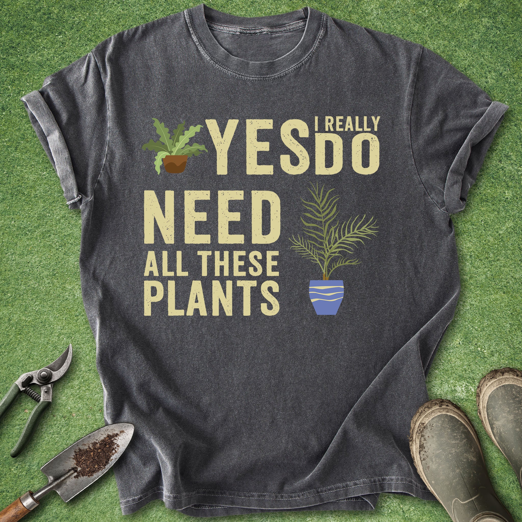 Gray t-shirt with 'I really need all these plants' text and plant graphics on a green grass background.
