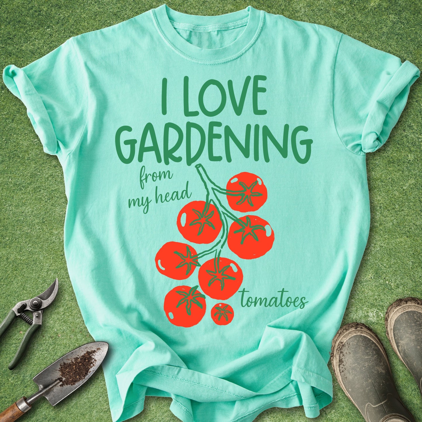 Mint green t-shirt with 'I love gardening from my head tomatoes' text and tomato graphics on a grass background.