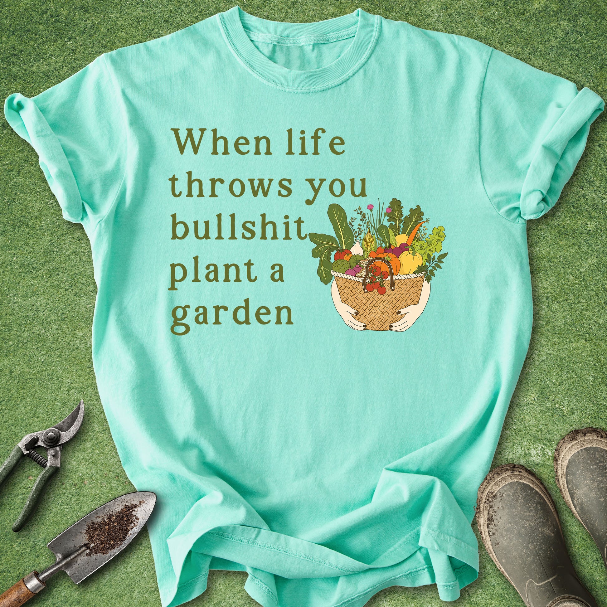 Mint green t-shirt with gardening graphic and text on a grass background