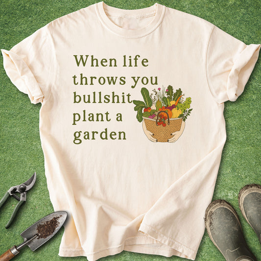 Funny gardening t-shirt with “When life throws you bullshit plant a garden” text and vegetable harvest basket illustration on ivory shirt