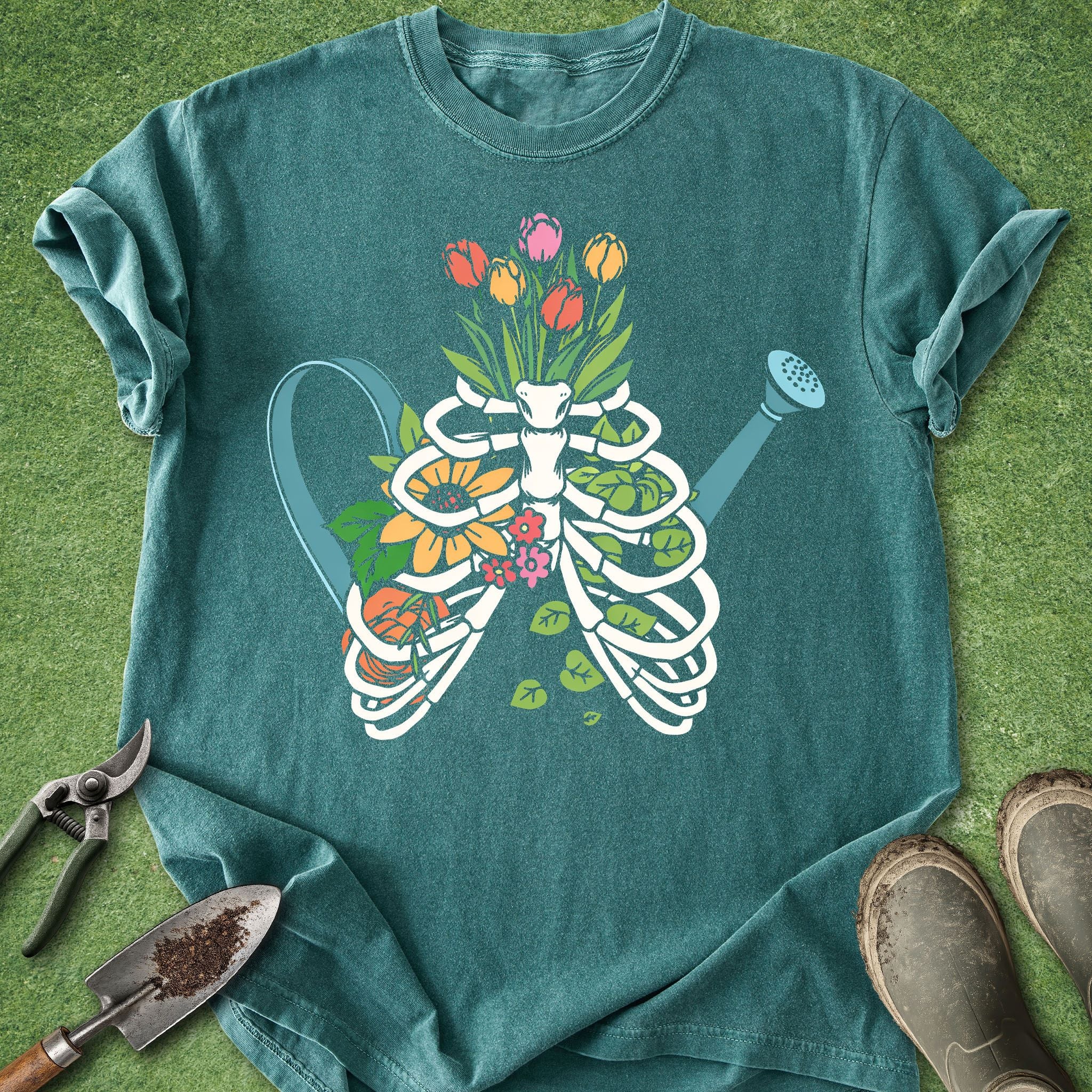 Teal t-shirt with a white skeleton ribcage design filled with colorful flowers on a grass background.