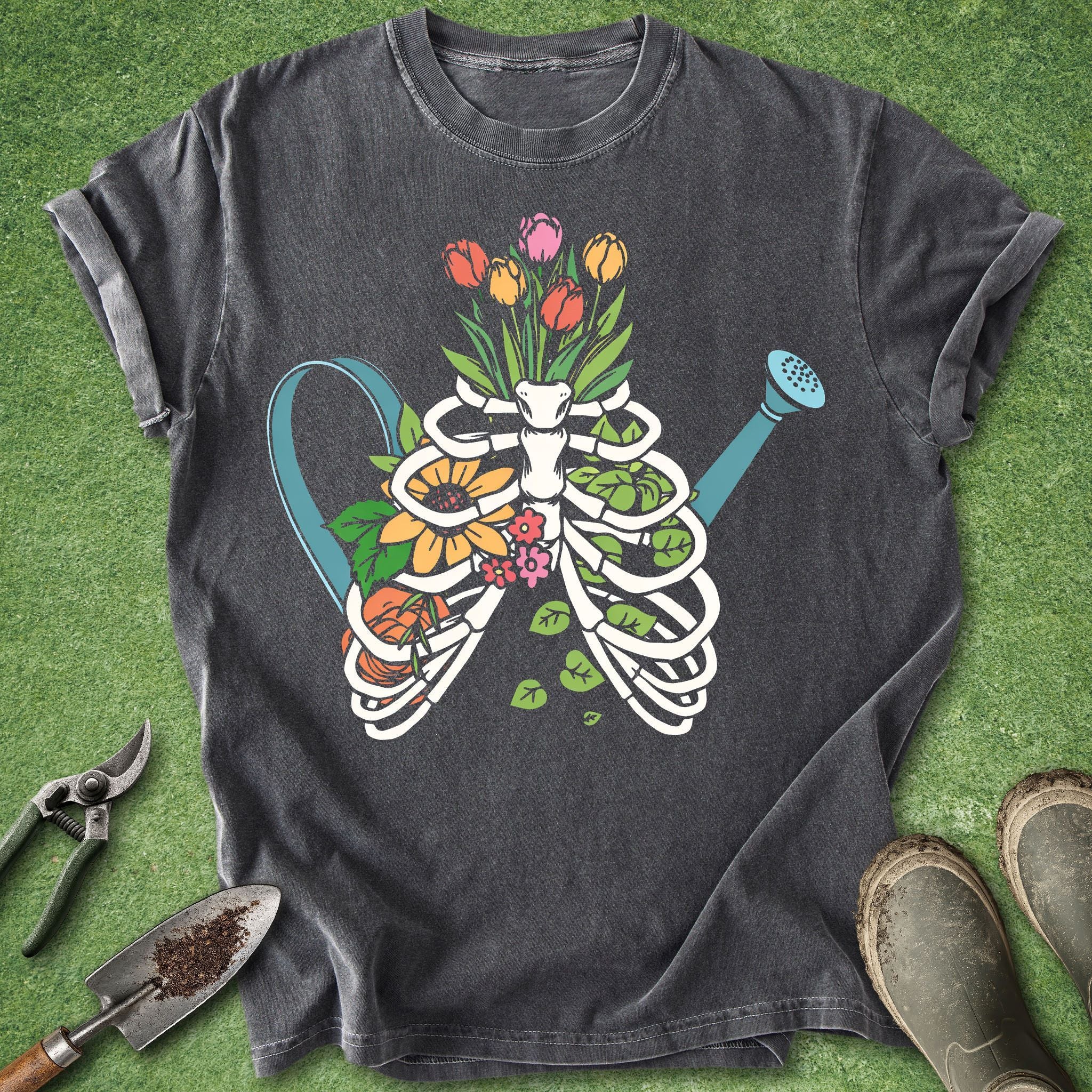 Dark gray t-shirt with a skeleton ribcage design filled with flowers and a shower head, on a grass background.