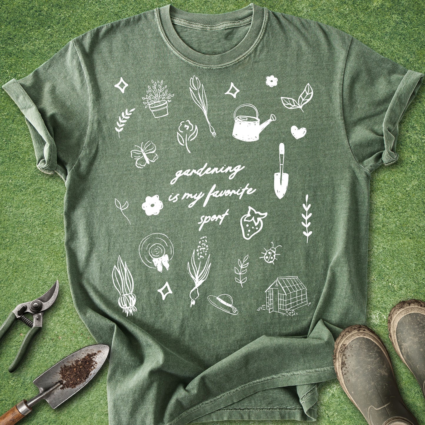 Comfort Colors Moss t-shirt featuring the phrase "Gardening Is My Favorite Sport" surrounded by hand-drawn gardening doodles including flowers, vegetables, tools, a watering can, greenhouse, and plants.