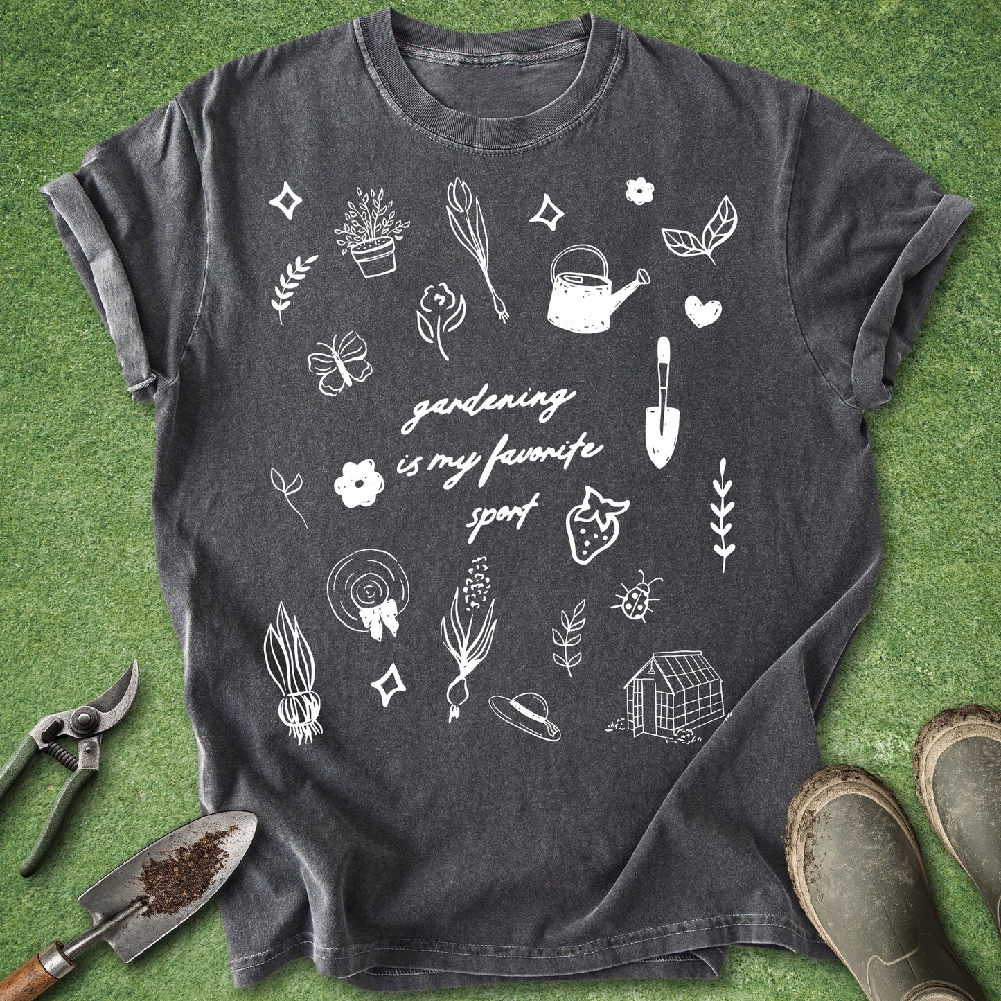 Comfort Colors Pepper t-shirt featuring the phrase "Gardening Is My Favorite Sport" surrounded by hand-drawn gardening doodles including flowers, vegetables, tools, a watering can, greenhouse, and plants.