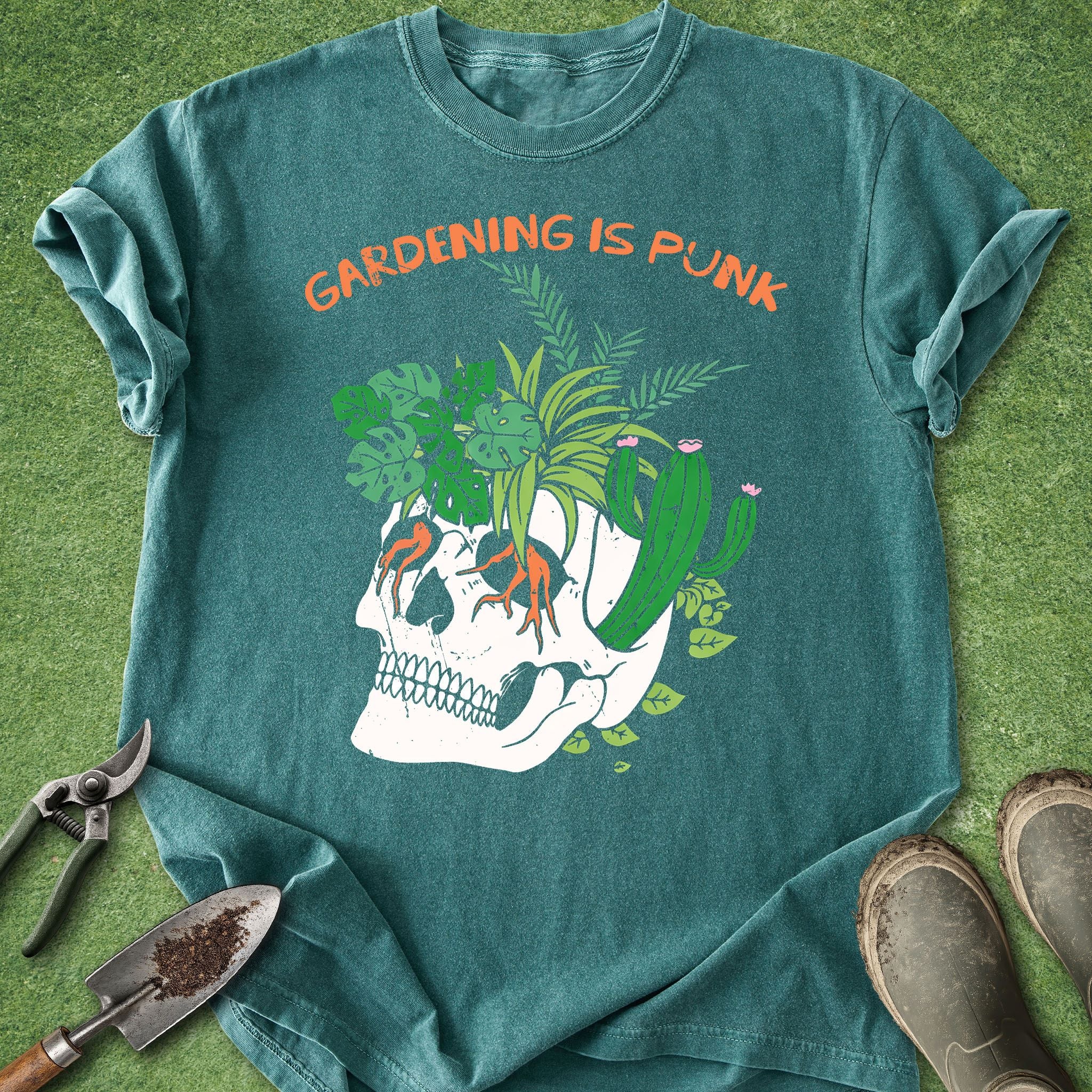 Teal t-shirt with skull and plants design and 'Gardening is Punk' text on a grass background.