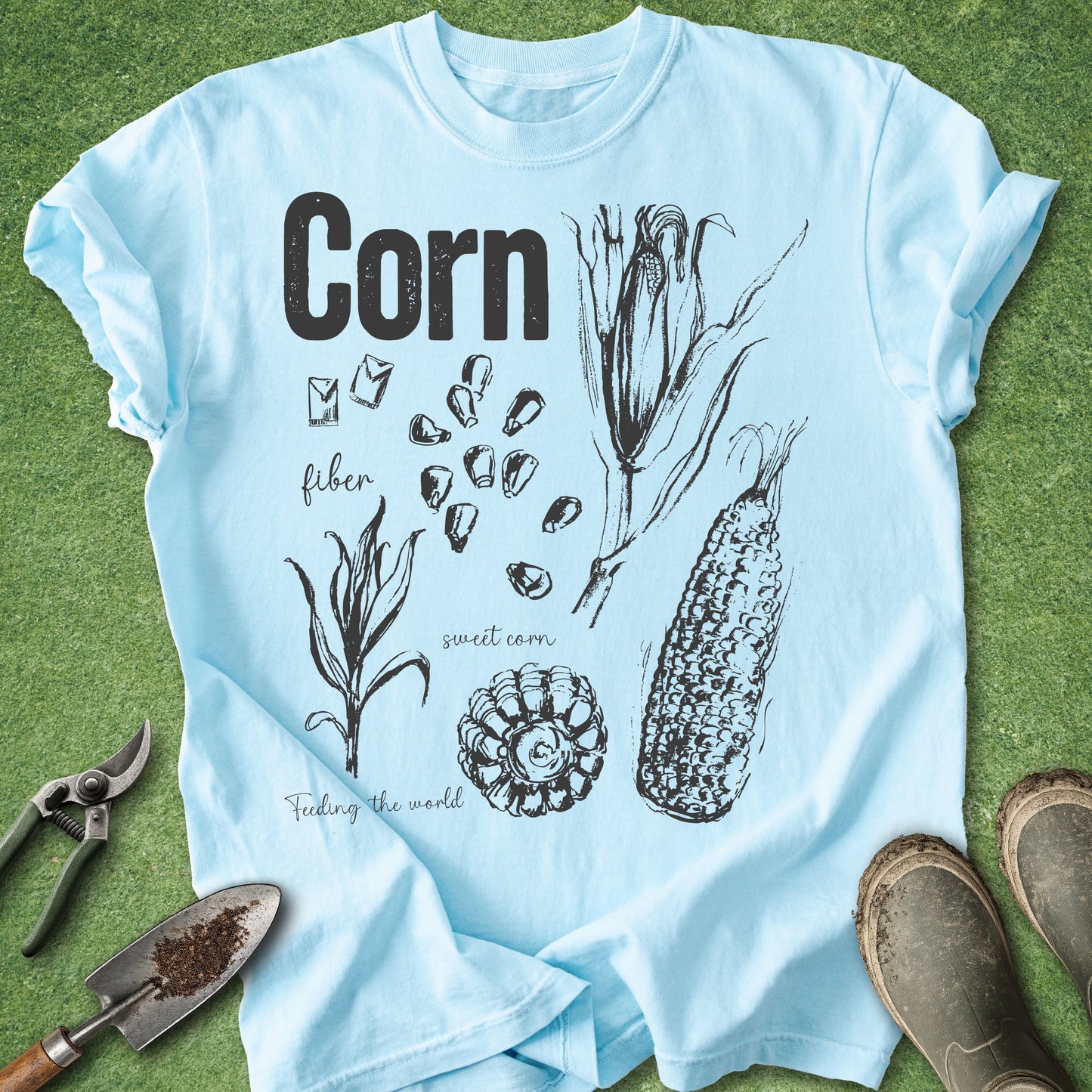 Light blue t-shirt with corn illustrations and text on a grass background