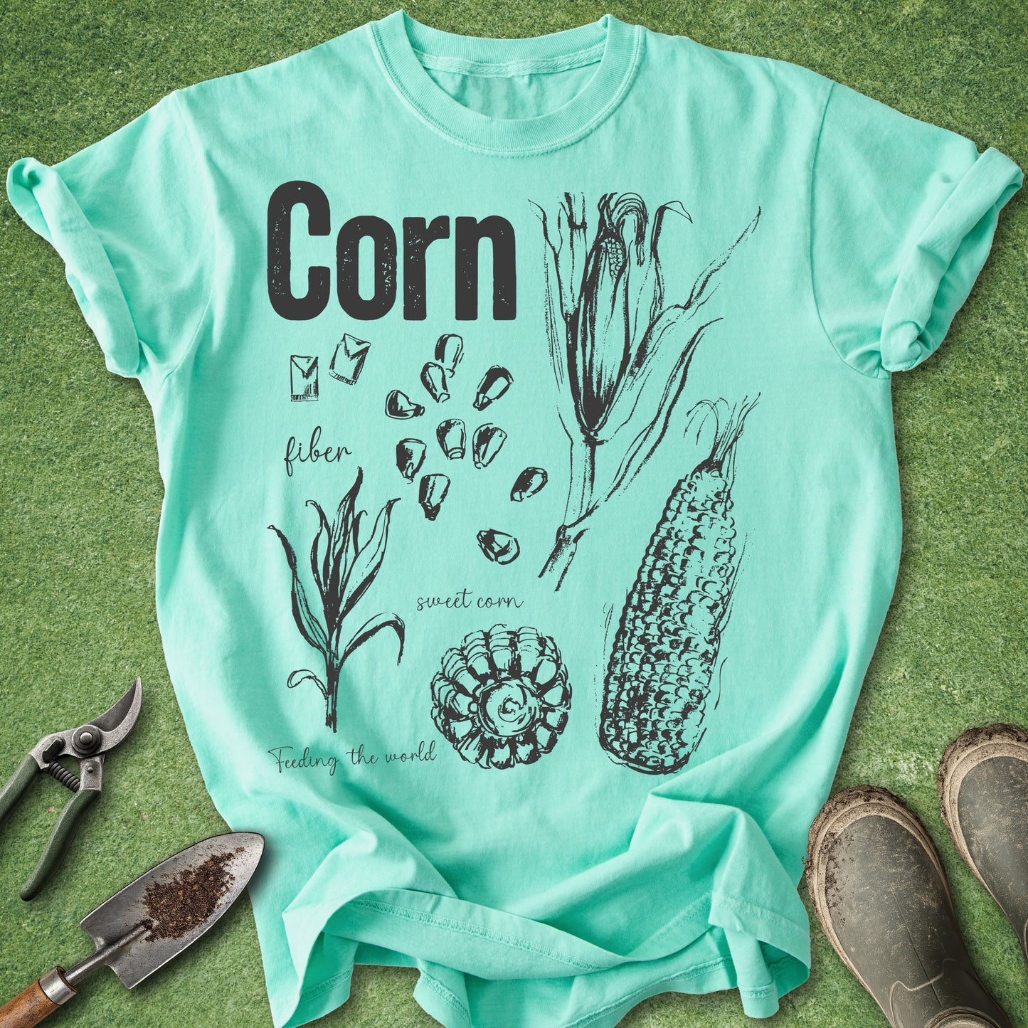Mint green t-shirt with corn illustration and text on a grass background