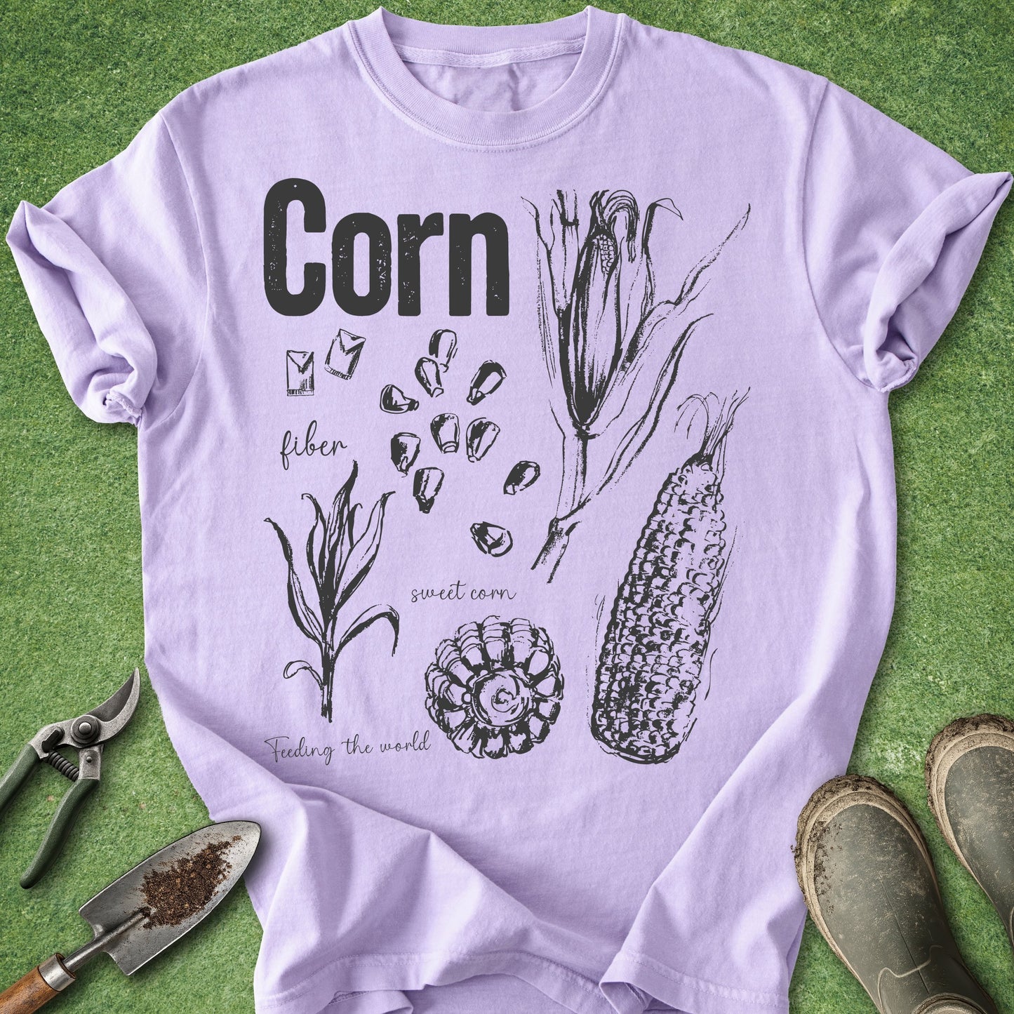 Purple t-shirt with corn illustration and text on a green grass background