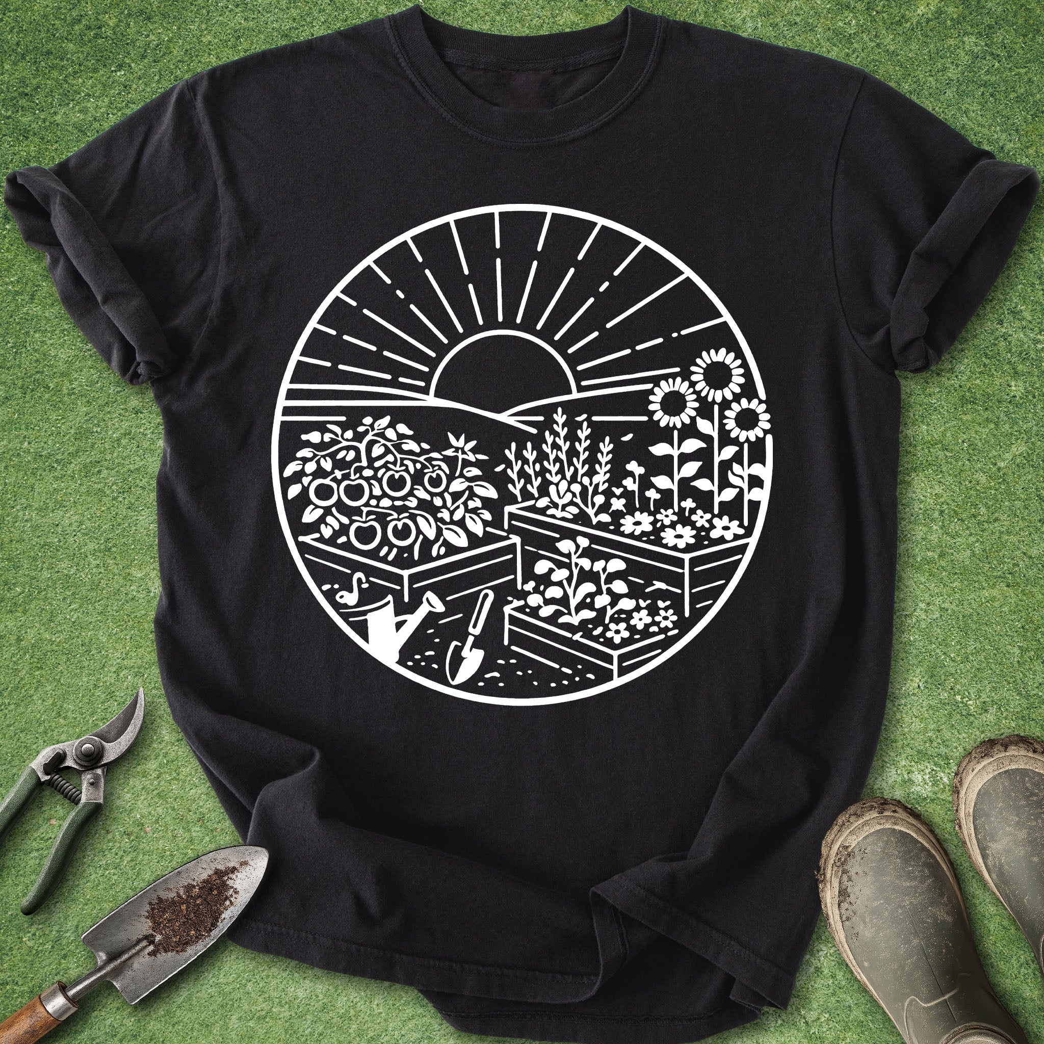 Black t-shirt with white garden graphic on a green surface with gardening tools.