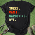 Black t-shirt with colorful text 'SORRY. CAN'T. GARDENING. BYE.' on a grass background with gardening tools.