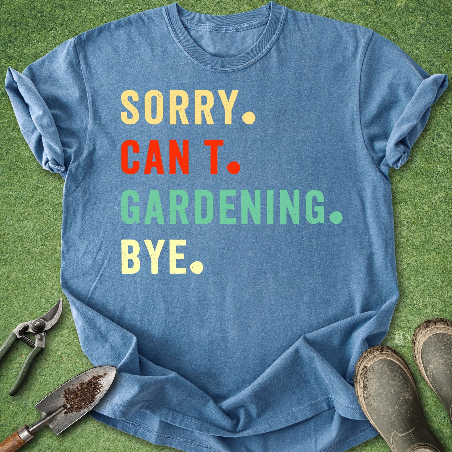 Blue t-shirt with colorful text on a grass background with gardening tools.