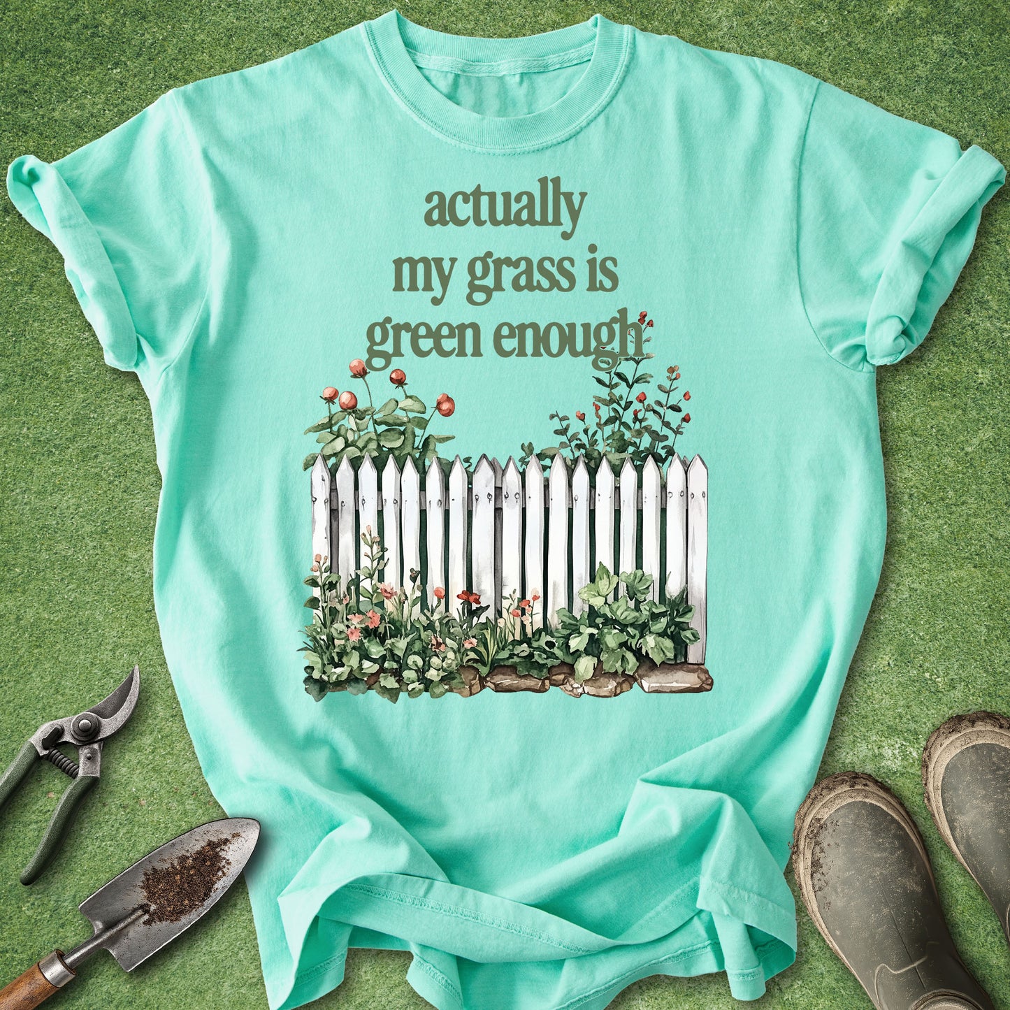 Watercolor-style garden design featuring a white picket fence, blooming flowers, and the phrase "Actually My Grass Is Green Enough" for gardeners and plant lovers.