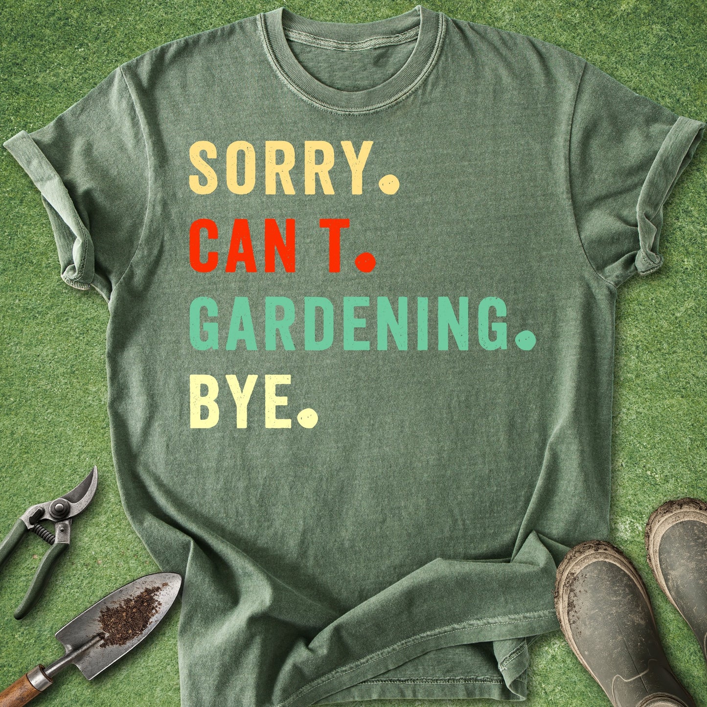 Green t-shirt with colorful text on a grass background with gardening tools.