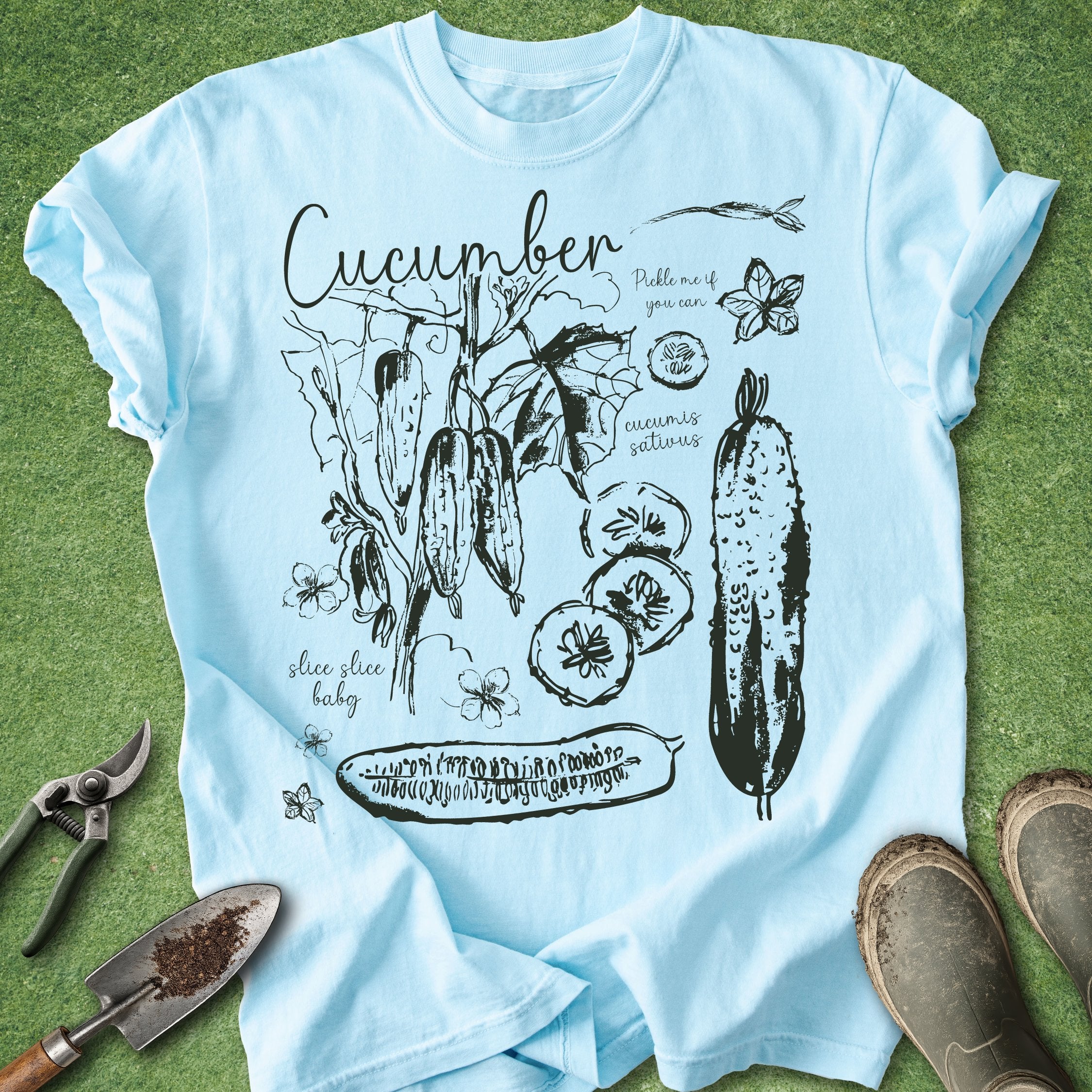 Light blue t-shirt with cucumber graphic design on a green grass background