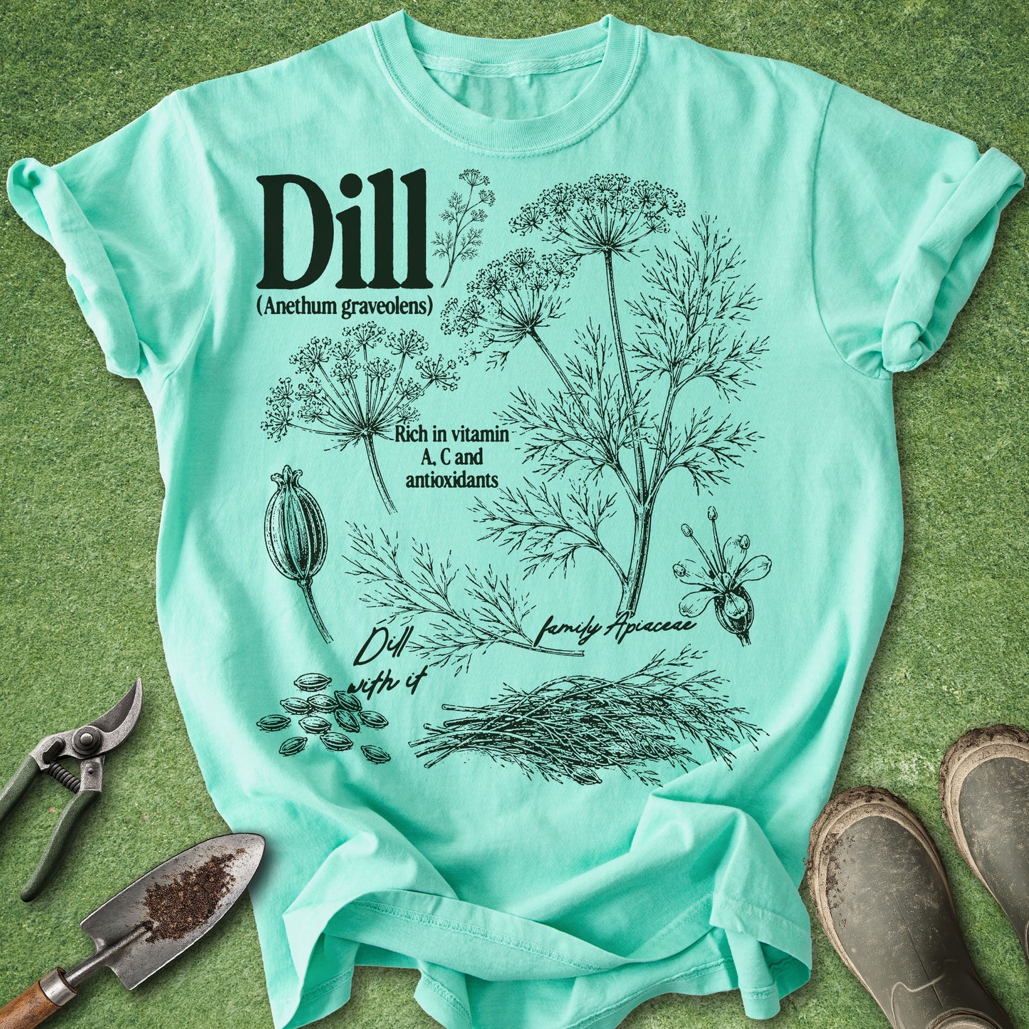Mint green t-shirt with dill plant illustration and text on a grass background