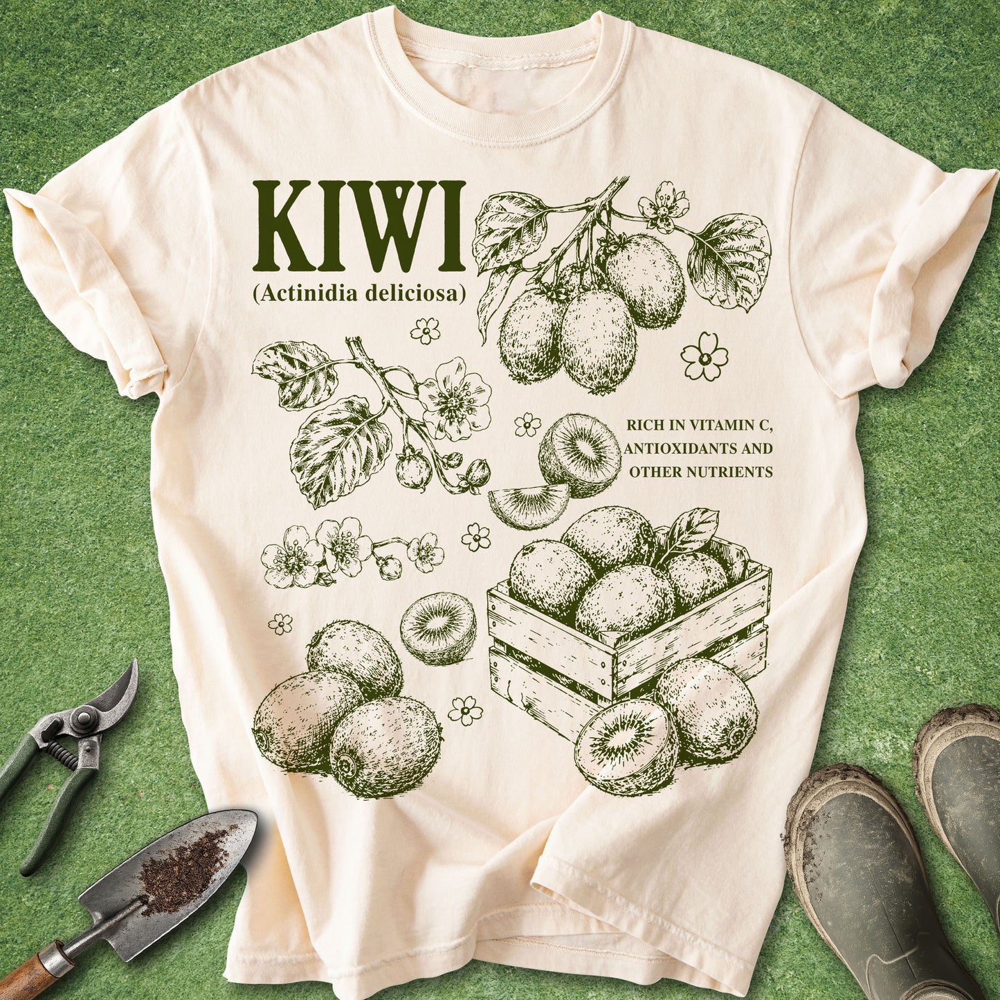 Ivory Comfort Colors t-shirt featuring vintage botanical kiwi fruit illustrations with kiwi vines, blossoms, leaves, sliced fruit, and harvested kiwis arranged in a natural history style design.