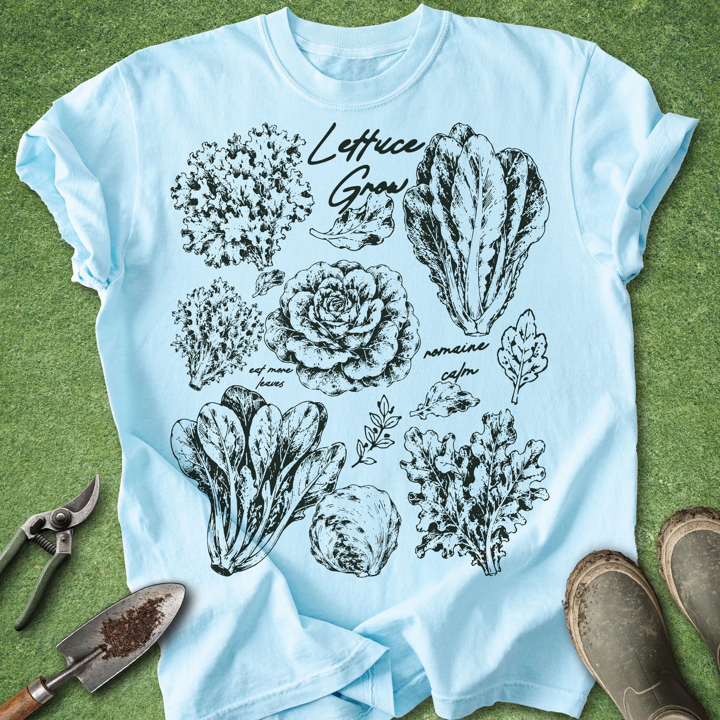 Light blue t-shirt with black vegetable illustrations on a green grass background