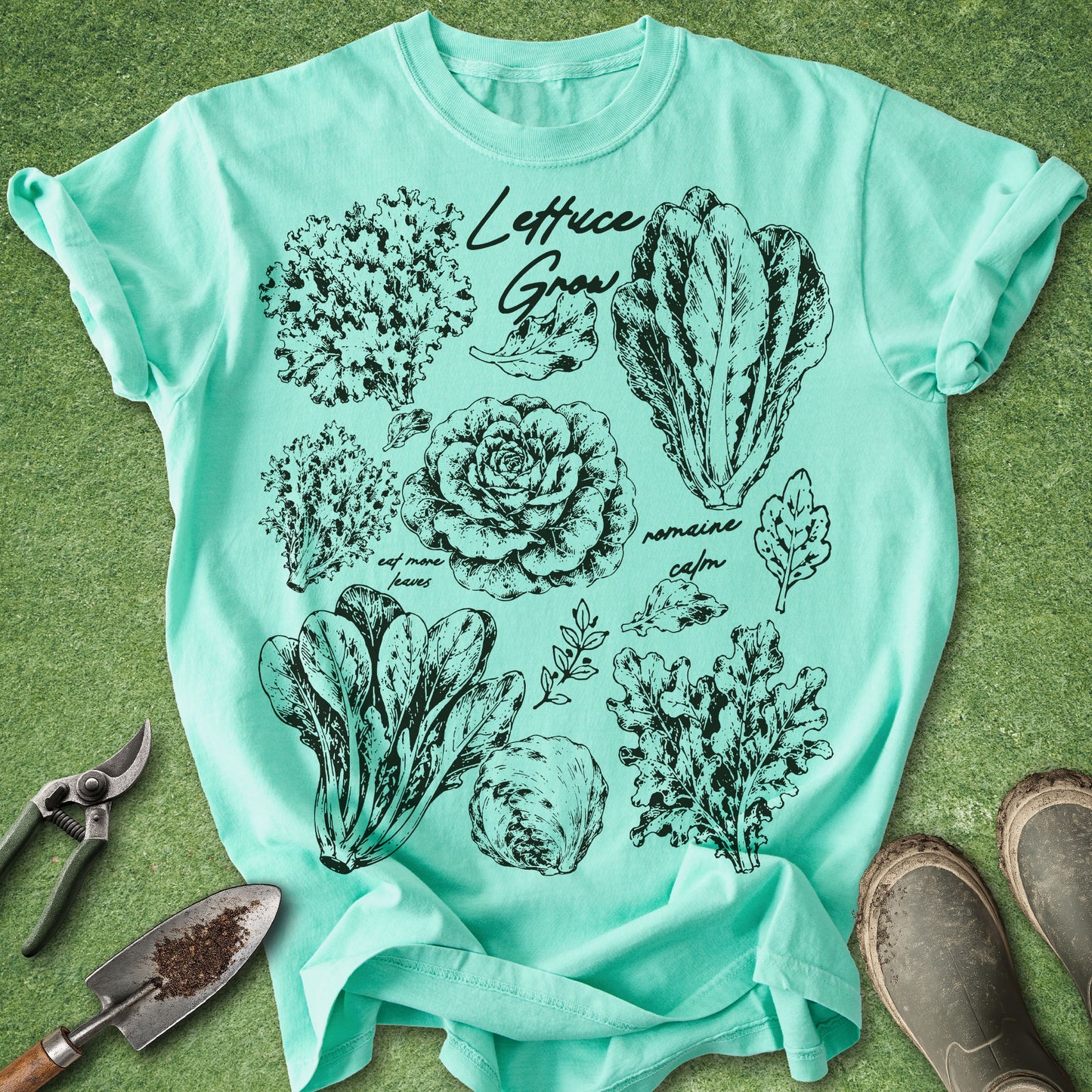 Mint green t-shirt with black botanical lettuce illustrations on a grassy background