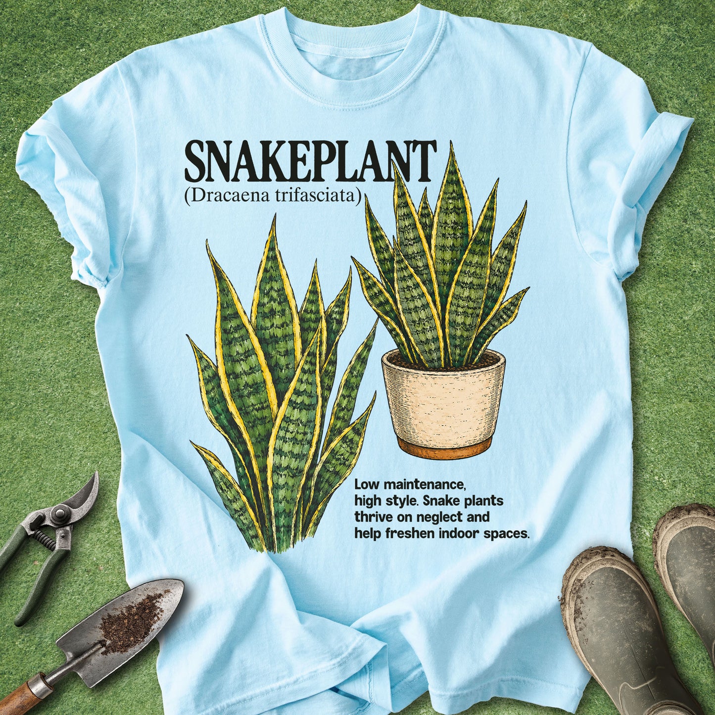 Light blue t-shirt with snake plant illustration and text on a green grass background