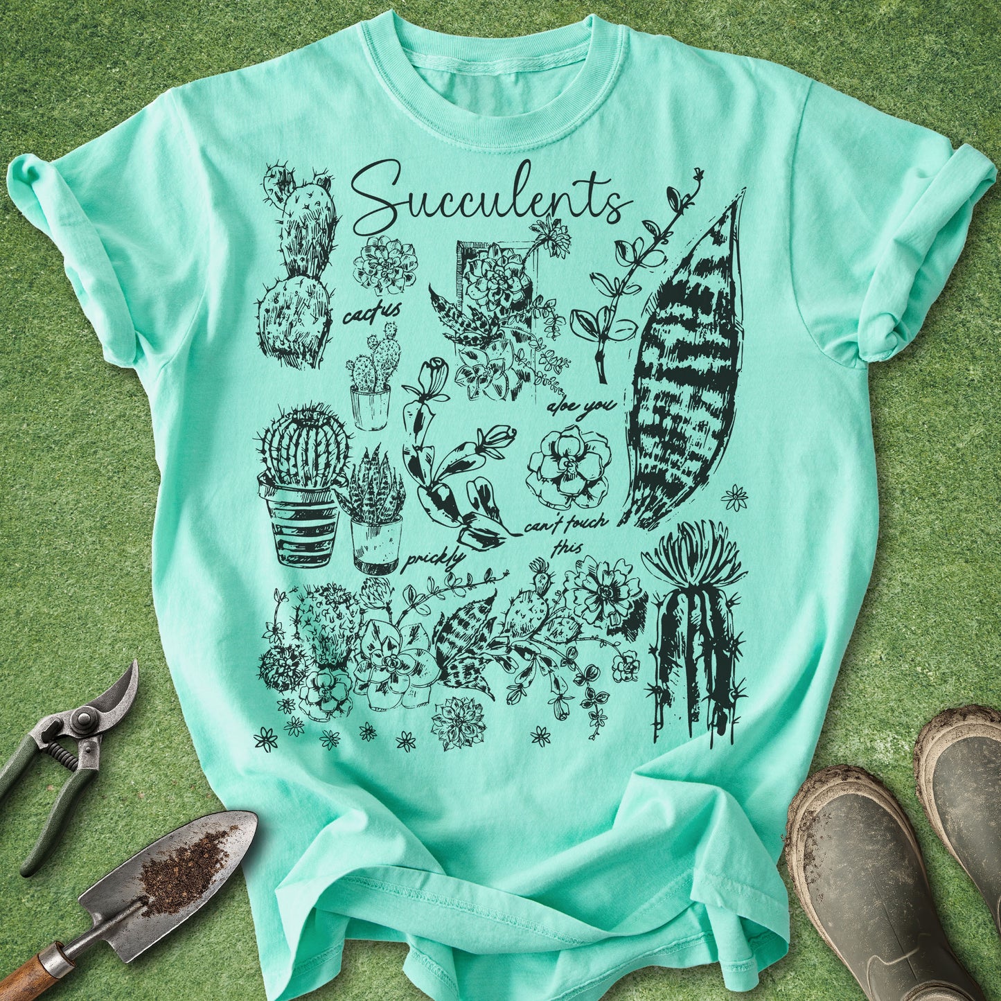 Mint green t-shirt with succulent illustrations on a grassy background
