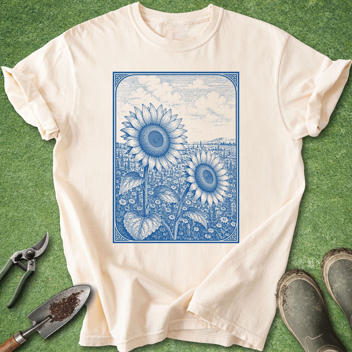 Vintage botanical t-shirt featuring two detailed blue sunflowers in a blooming wildflower field with an engraved illustration style framed by an ornamental border on an ivory shirt.