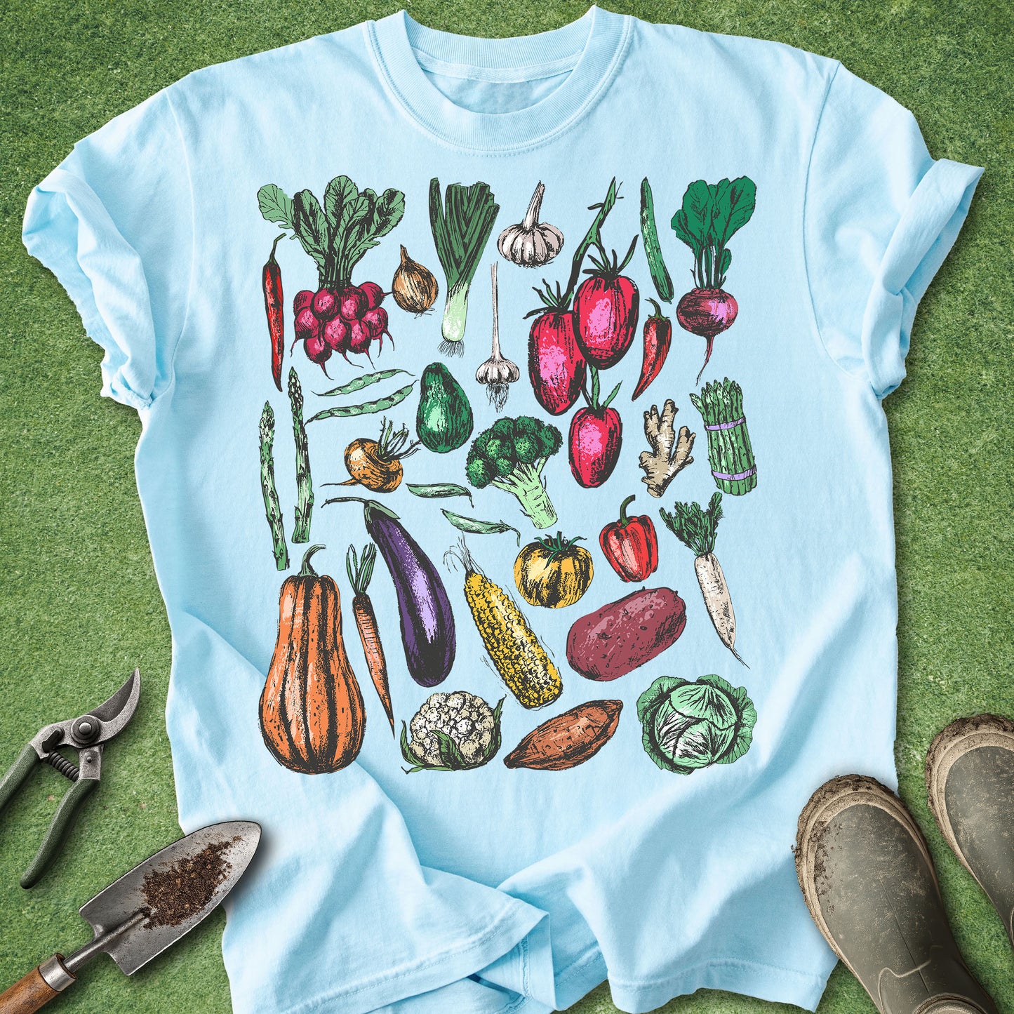 Light blue t-shirt with colorful vegetable illustrations on a green grass background