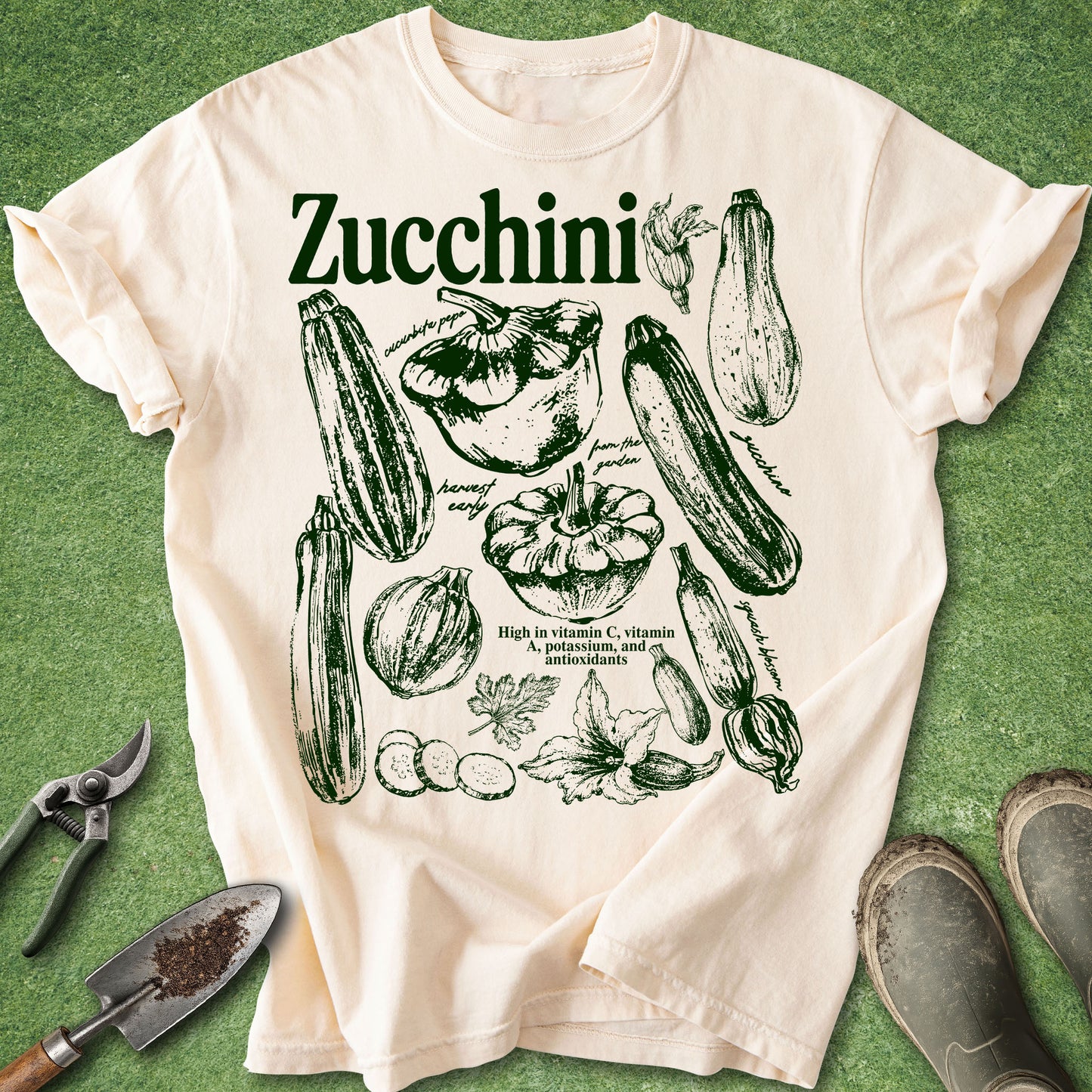 Ivory Comfort Colors t-shirt featuring vintage botanical zucchini illustrations with blossoms, leaves, sliced zucchini, and heirloom varieties arranged in a garden journal style design.