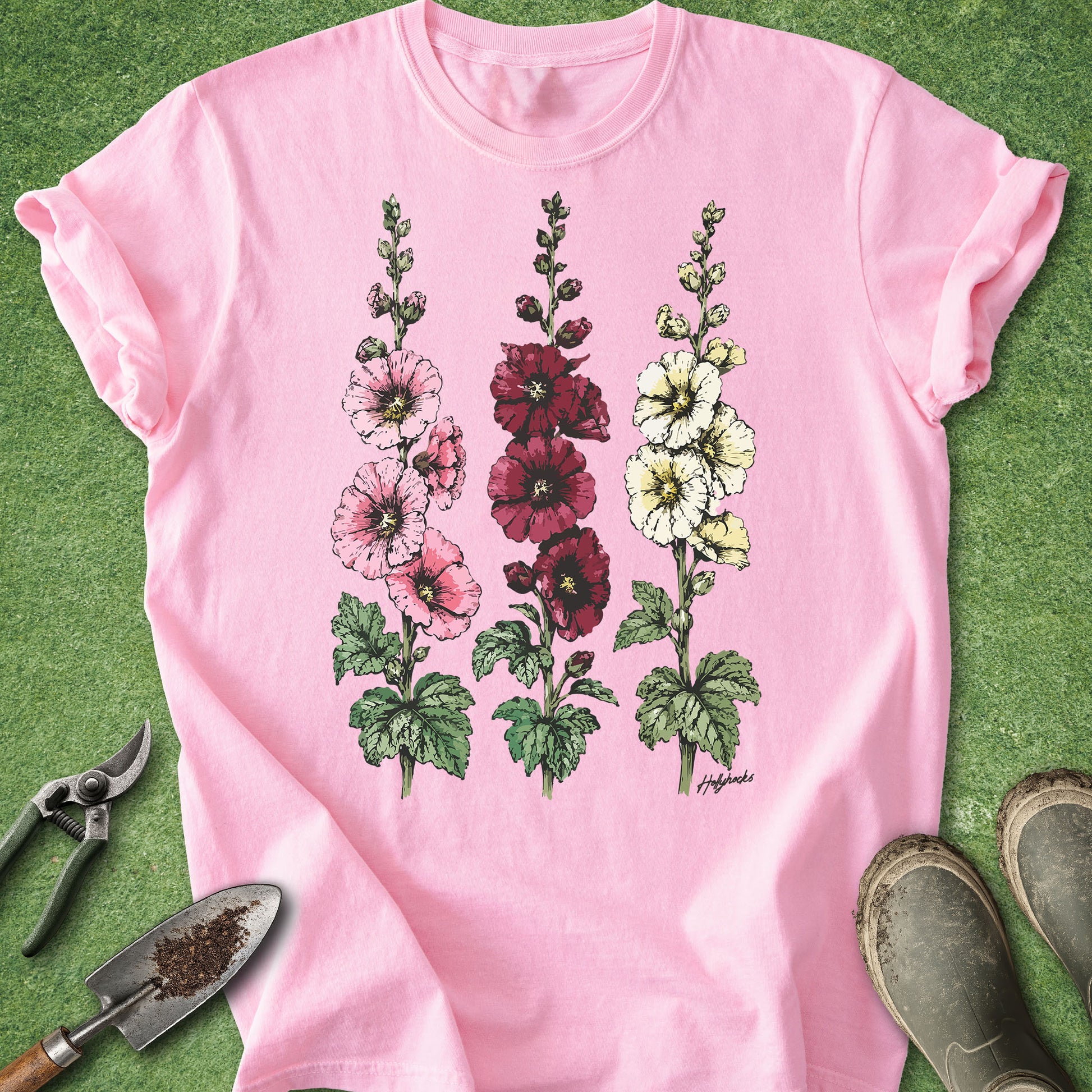  Blossom Comfort Colors t-shirt featuring detailed botanical illustrations of three blooming hollyhock flowers in pink, burgundy, and white with green foliage in a vintage botanical style.