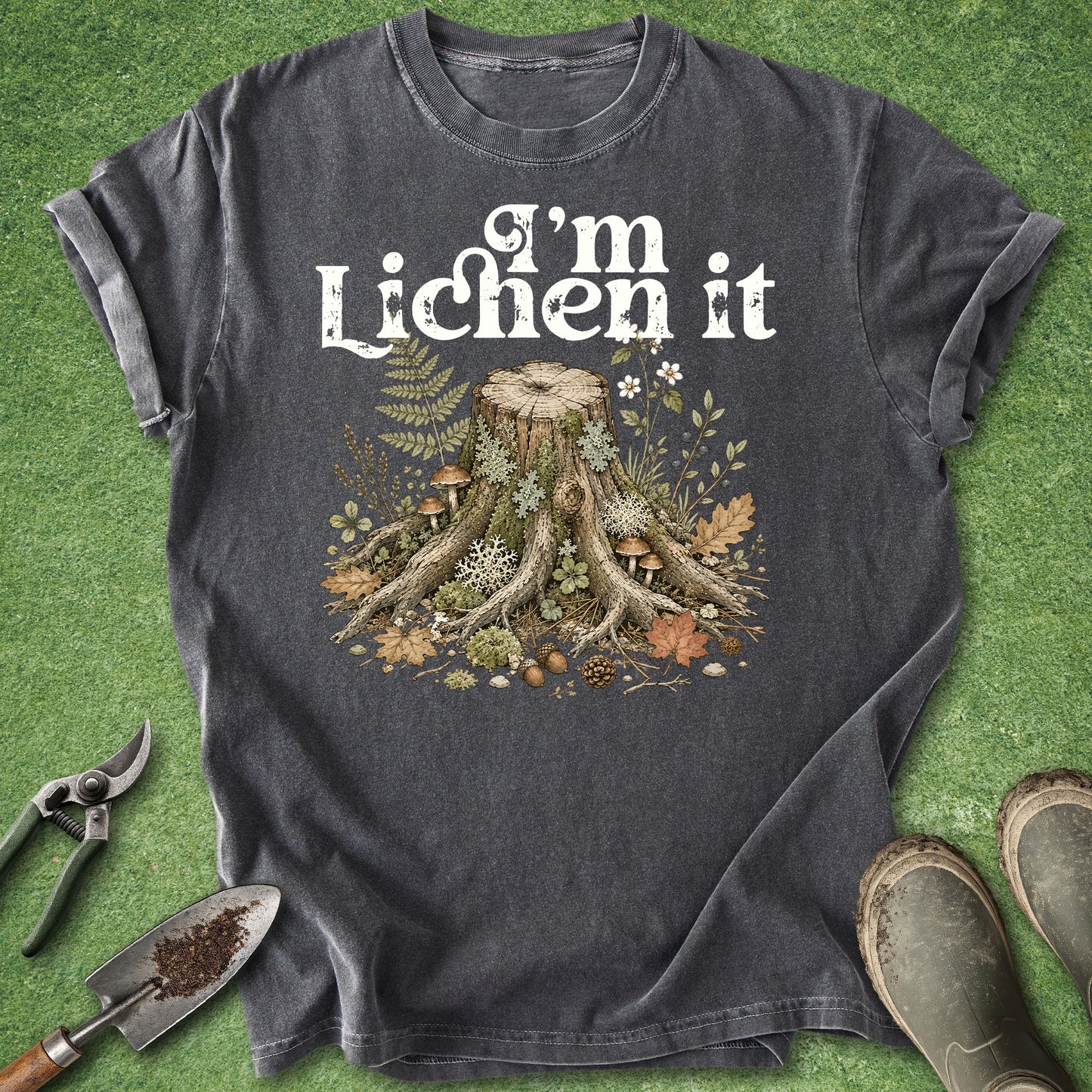 Pepper gray t-shirt featuring the phrase "I'm Lichen It" above a detailed vintage-style illustration of a woodland tree stump surrounded by moss, lichens, mushrooms, ferns, leaves, and forest plants.