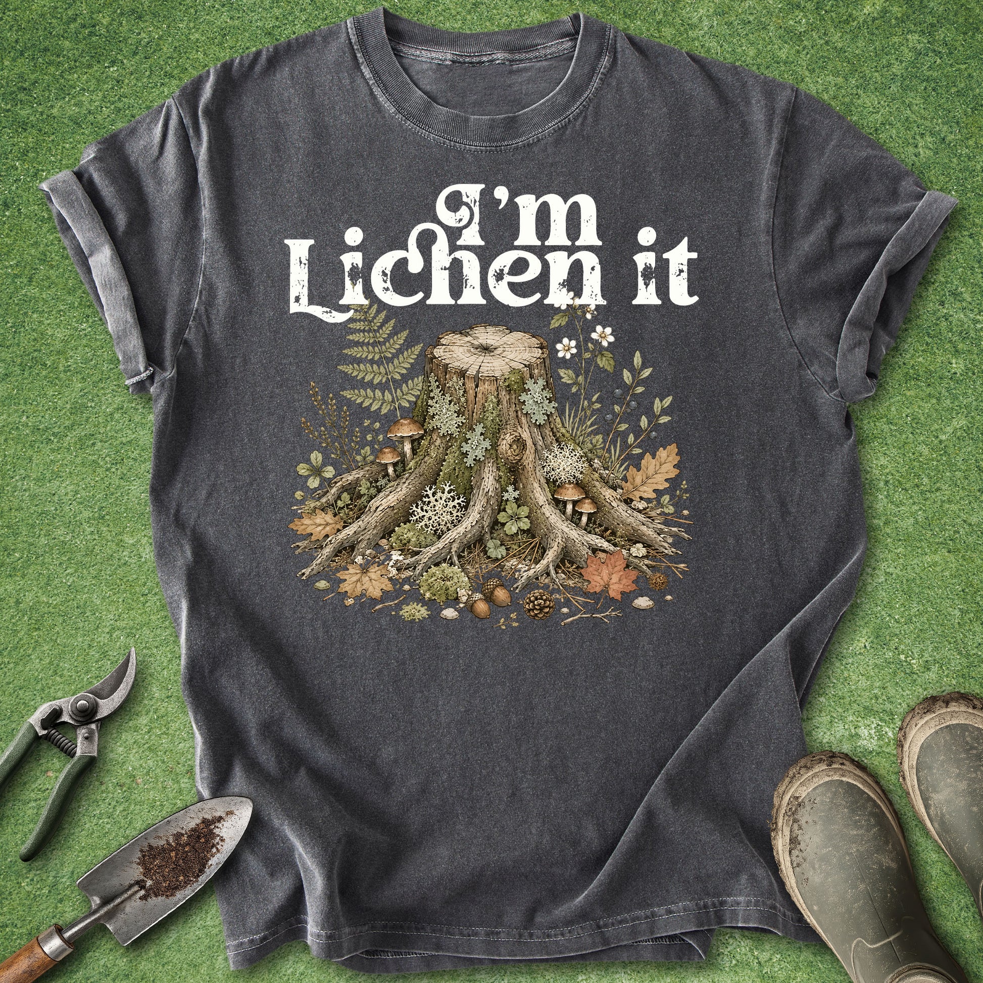 Pepper gray t-shirt featuring the phrase "I'm Lichen It" above a detailed vintage-style illustration of a woodland tree stump surrounded by moss, lichens, mushrooms, ferns, leaves, and forest plants.