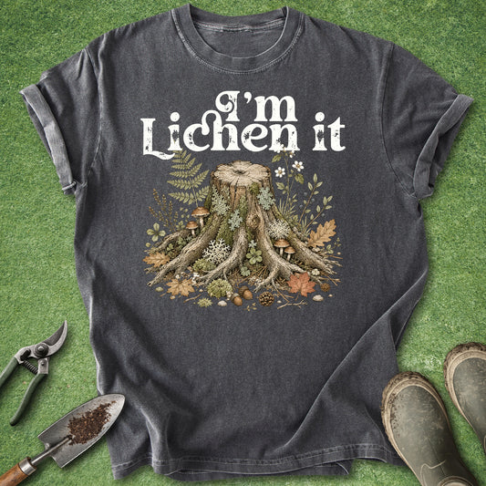 Pepper gray t-shirt featuring the phrase "I'm Lichen It" above a detailed vintage-style illustration of a woodland tree stump surrounded by moss, lichens, mushrooms, ferns, leaves, and forest plants.