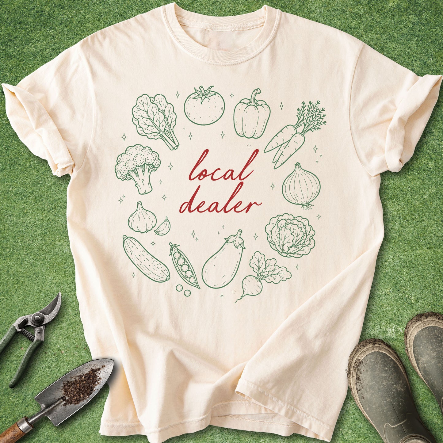 Ivory Comfort Colors t-shirt featuring the phrase "local dealer" surrounded by hand-drawn vegetables including tomatoes, peppers, carrots, onions, broccoli, garlic, cucumbers, peas, cabbage, eggplant, and leafy greens.
