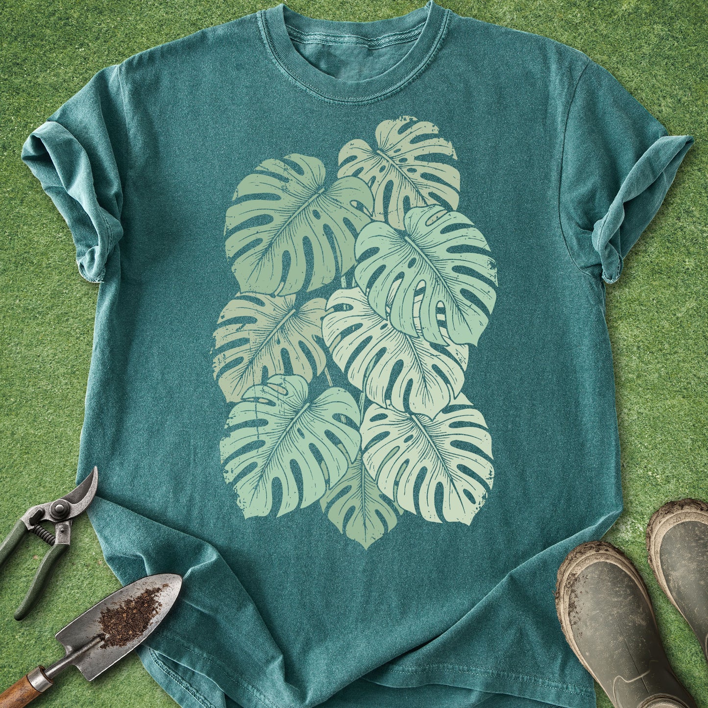 Teal t-shirt with leaf design on a grassy background