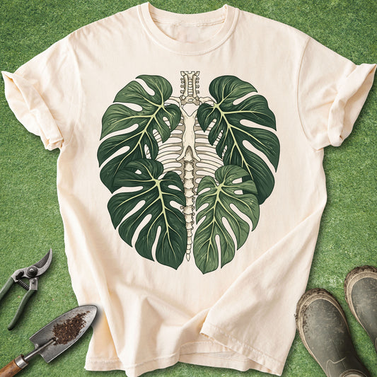 Ivory t-shirt featuring a detailed botanical anatomy illustration of a human rib cage surrounded by four large Monstera leaves.